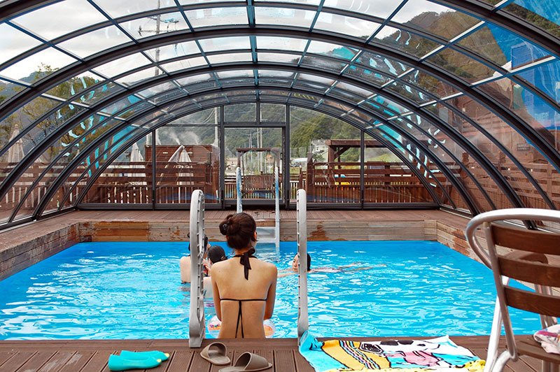 A family swimming In a pool with a retractable enclosure